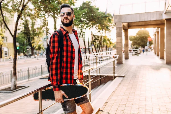 Kablosuz kulaklık bir sakallı şık adam şehir etrafında bir kaykay ile yürüyor