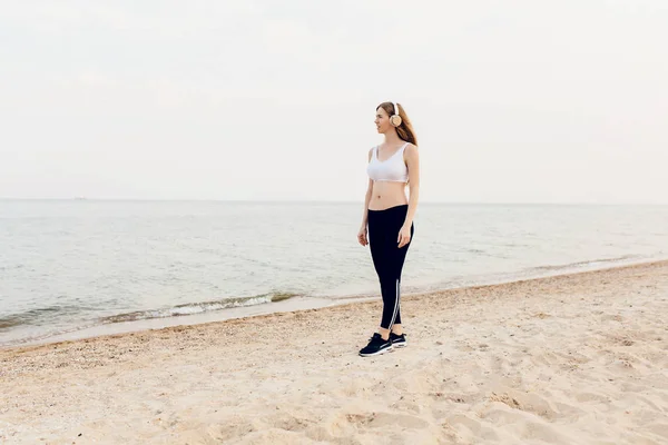 Beautiful athletic girl walking on the sea and listening to musi — Stock Photo, Image