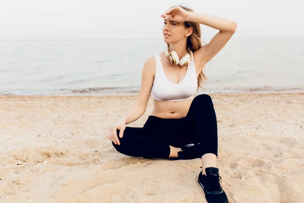 스포티 한 소녀 앉아 에 이 바닷가 과 듣기 음악 에 머리 — 스톡 사진