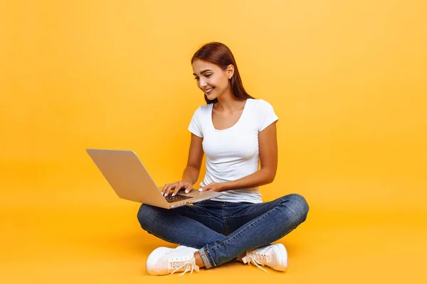 Junge Frau sitzt im Schneidersitz mit Laptop isoliert auf gelb — Stockfoto