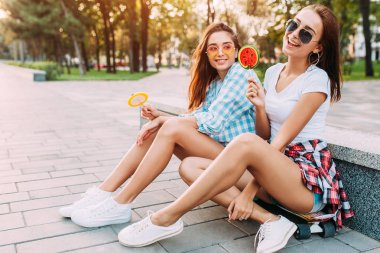 Lolipop h ile bir kaykay üzerinde oturan iki genç şık kadın