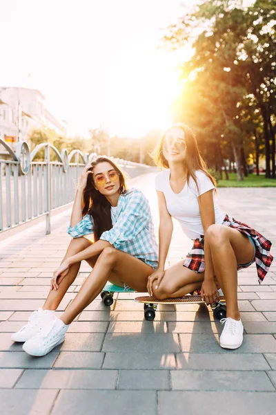 Dvě stylové mladé dívky, které sedí se skateboardy v parku — Stock fotografie