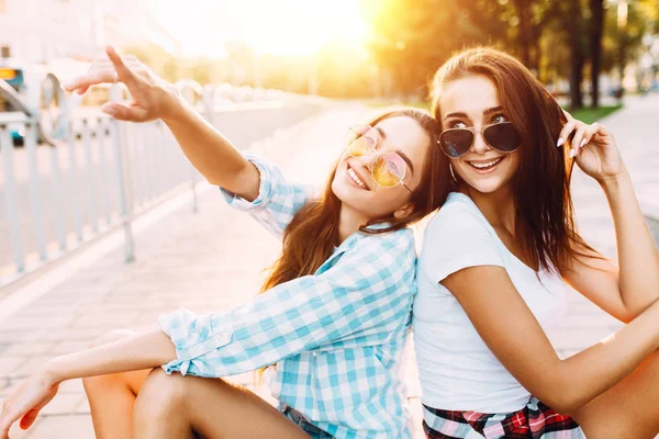 Due giovani ragazze in occhiali da sole, rilassarsi e divertirsi seduti o — Foto Stock