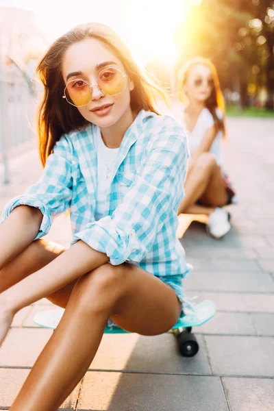 Dos chicas jóvenes y elegantes sentadas con patinetas en el parque —  Fotos de Stock