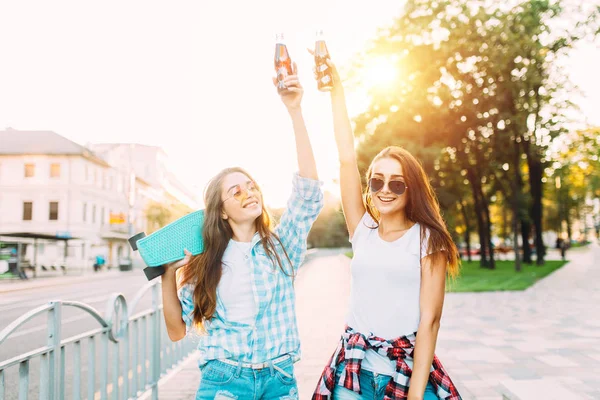 Duas namoradas de óculos de sol, bebem uma bebida e descem um citadino — Fotografia de Stock