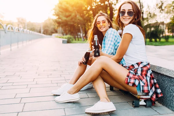 Dos chicas con ropa casual y gafas de sol sentadas en el parque o —  Fotos de Stock