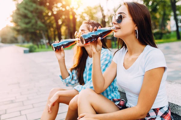 Duas meninas de roupas casuais e óculos de sol, sentadas no Parque — Fotografia de Stock