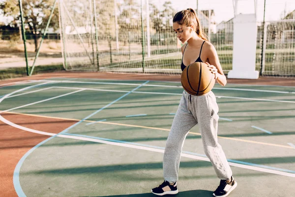 Schöne junge sportliche Mädchen spielt mit dem Ball auf dem Korb — Stockfoto