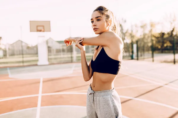 Atractiva joven atlética en ropa deportiva haciendo ejercicios de estiramiento del brazo al aire libre — Foto de Stock