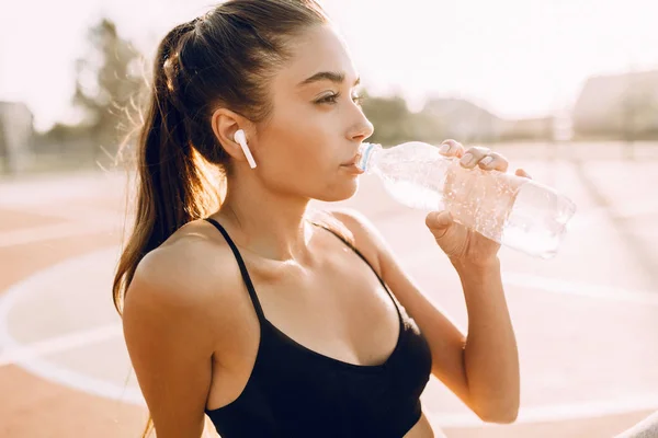 Atletische jong meisje drinken van water uit een fles na een training — Stockfoto