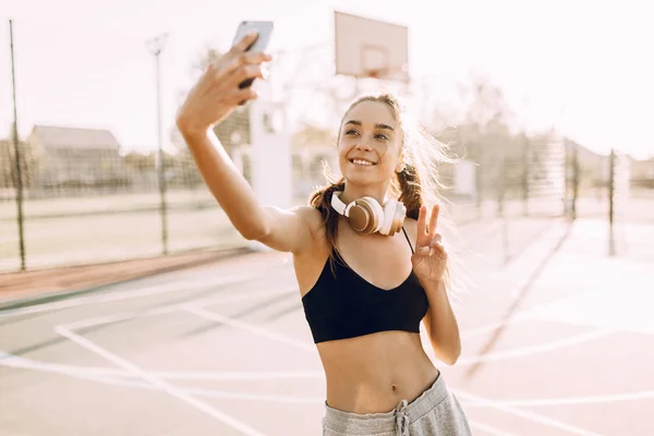 스포츠를하는 동안 야외에서 셀카를 찍는 헤드폰을 가진 행복한 피트니스 소녀 — 스톡 사진