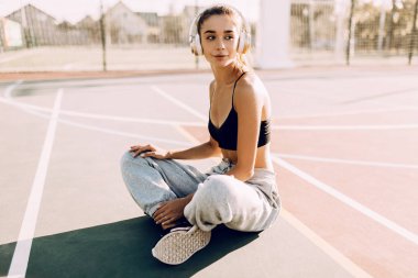 Kulaklıkla müzik dinlerken açık havada poz veren çekici atletik genç kadın. Antrenmandan sonra