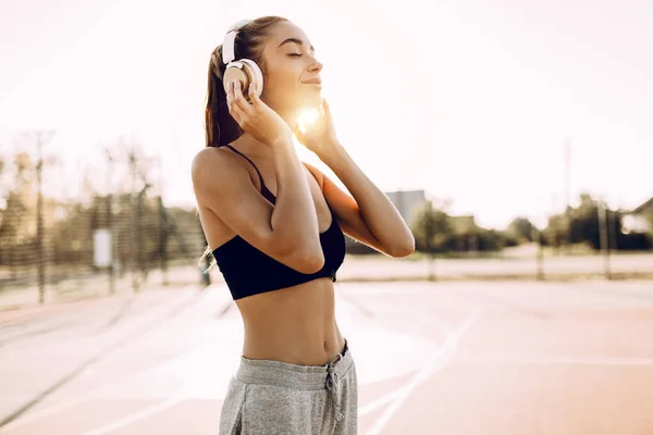 Gelukkige atletische jonge vrouw, in sportkleding, buiten staan en luisteren naar muziek met een koptelefoon — Stockfoto