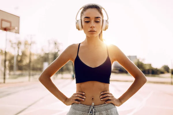 Gelukkige atletische jonge vrouw, in sportkleding, buiten staan en luisteren naar muziek met een koptelefoon — Stockfoto