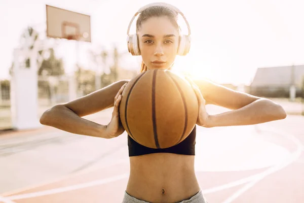 Imagen de la hermosa joven mujer de fitness deportivo increíble posando con baloncesto al aire libre . — Foto de Stock