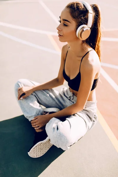 Aantrekkelijke atletische jonge vrouw poseren buitenshuis terwijl ze naar muziek luistert met een koptelefoon. Na een training — Stockfoto