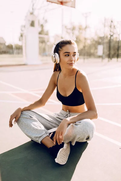 Atractiva joven atlética posando al aire libre mientras escucha música con auriculares. Después de un entrenamiento — Foto de Stock