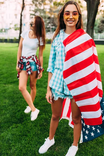 Due ragazze attraenti alla moda con una bandiera americana, in posa in th — Foto Stock