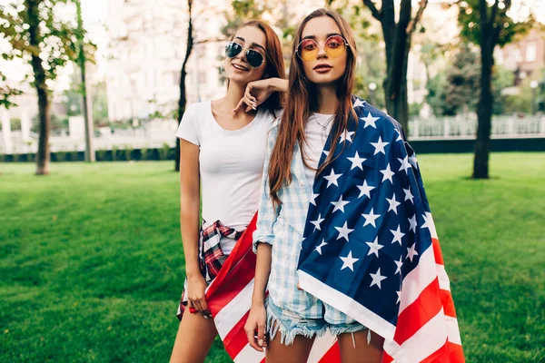 Due ragazze attraenti alla moda con una bandiera americana, in posa in th — Foto Stock