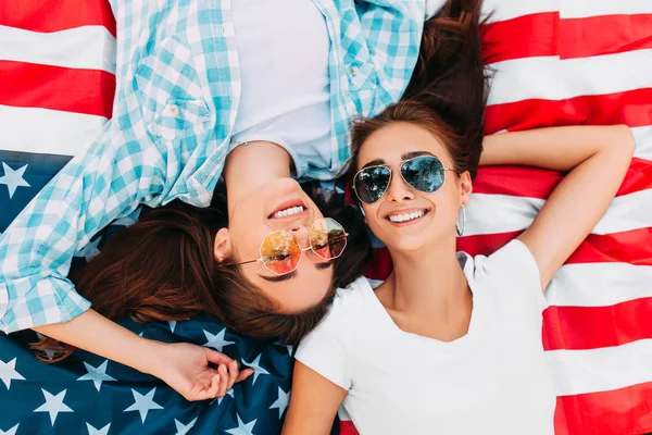 Dwie atrakcyjne młode dziewczyny zrelaksować się na flagi USA na zewnątrz. Dzień Niepodległości — Zdjęcie stockowe
