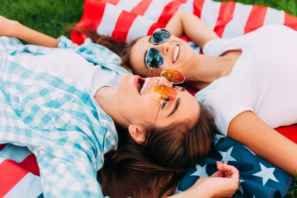Δύο ελκυστικά νεαρά κορίτσια χαλαρώνουν στη σημαία των ΗΠΑ σε εξωτερικούς χώρους. Ημέρα ανεξαρτησίας — Φωτογραφία Αρχείου