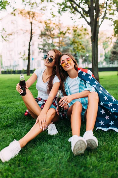 Due giovani ragazze attraenti in occhiali da sole seduti nel parco su — Foto Stock