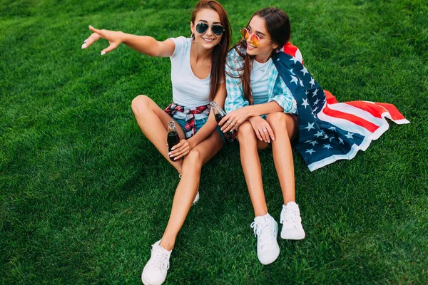 Due giovani ragazze attraenti in occhiali da sole seduti nel parco su — Foto Stock