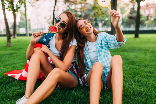 Dvě atraktivní mladé dívky na slunečních brýlích, které sedí v parku na — Stock fotografie