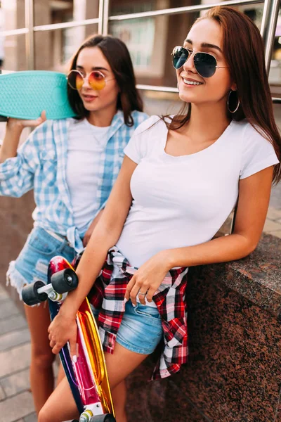 Due giovani ragazze attraenti in posa occhiali da sole con skateboard in città — Foto Stock