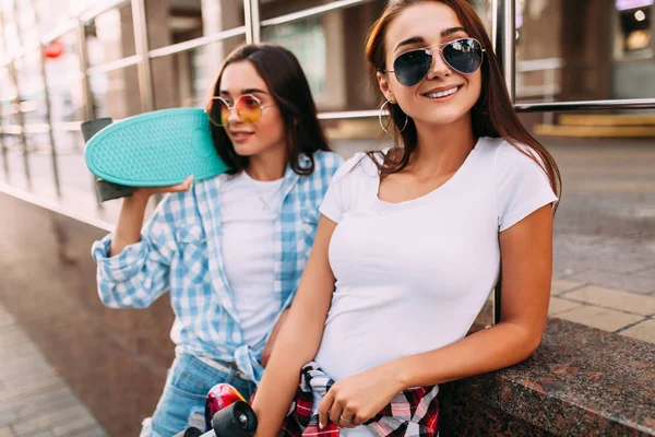 Dos chicas jóvenes atractivas en gafas de sol posan con monopatines en la ciudad — Foto de Stock