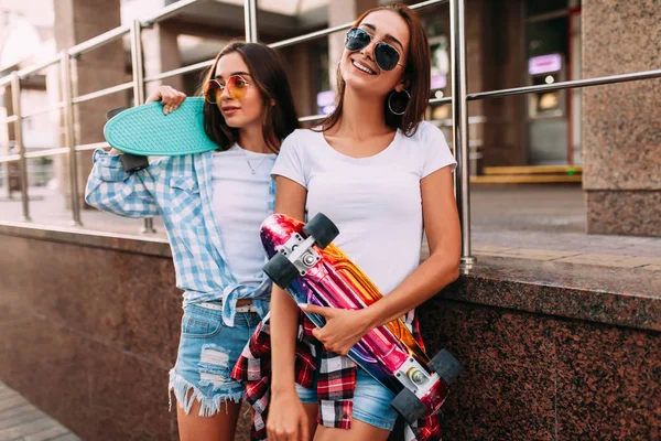 Dos chicas jóvenes atractivas en gafas de sol posan con monopatines en la ciudad —  Fotos de Stock
