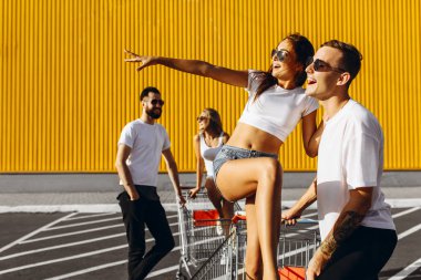Beyaz t-shirt genç bir grup, mağaza, süpermarket yakınındaki arabaları eğlenceli binmek, arkadaşlar Güneşli havalarda açık havada eğlenin