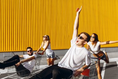 Alışveriş arabalarında eğlenen bir grup mutlu genç, alışveriş arabasına biniyor. güneş ışığı ile yaz günü.