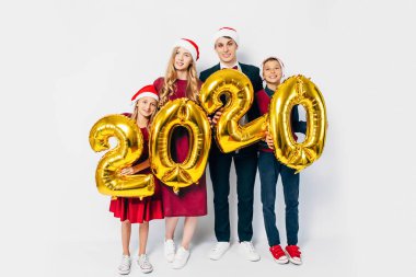 Çocuklu mutlu bir aile Noel Baba şapkası takıyor ellerinde balonlar