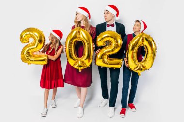 Çocuklu mutlu bir aile Noel Baba şapkası takıyor ellerinde balonlar