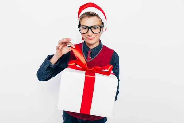 Gelukkige jongen met een rode kerstmuts. Stijlvolle jongen met kerstcadeau, opent vrolijk kerstcadeau, op witte achtergrond — Stockfoto