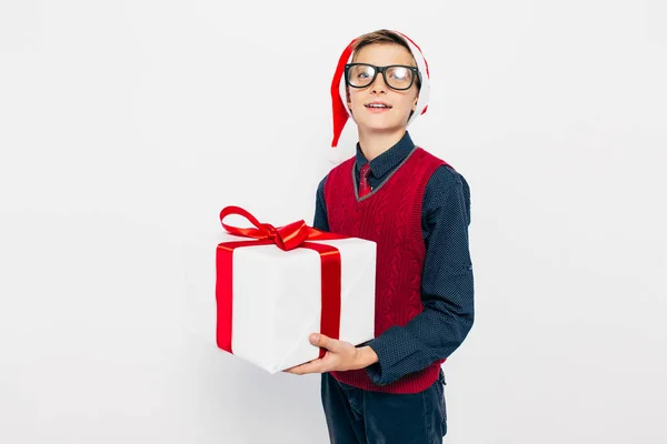 Grappig jongetje met een rode kerstmuts. Stijlvolle jongen met kerstcadeau, op witte achtergrond. — Stockfoto