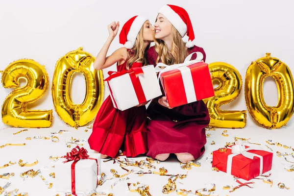 Fröhliche Mutter und ihre süße Tochter in Weihnachtsmützen, die Geschenke austauschen. ein Elternteil und ein kleines Kind haben Spaß auf weißem Hintergrund, mit Luftballons in Form von Figuren 2020. — Stockfoto