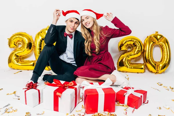 Jovem família, cara e menina em chapéus de Papai Noel, se divertindo com presentes de Natal sentado no fundo branco — Fotografia de Stock