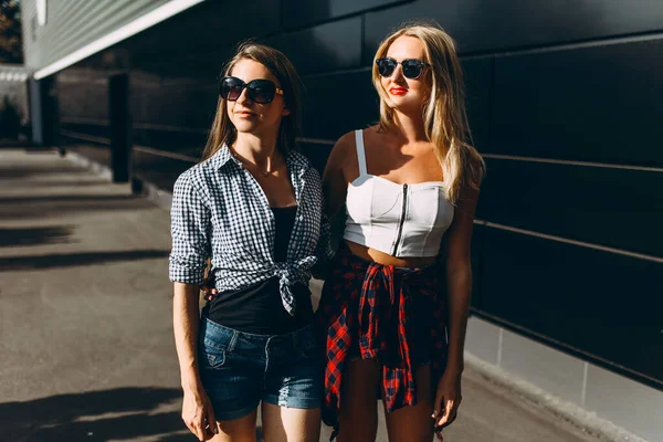 Di due amiche ridenti in occhiali da sole che passano il loro tempo libero insieme passeggiando per la città — Foto Stock