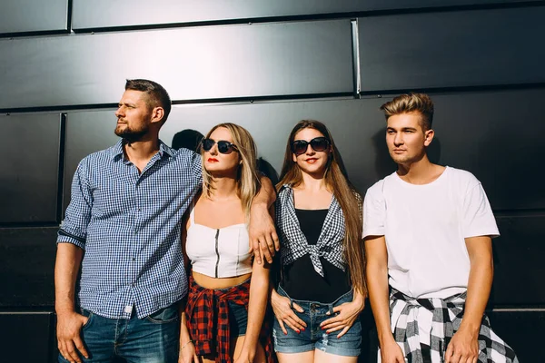 Un grupo de jóvenes y elegantes amigos, chicas y chicos posando juntos contra una pared negra en la ciudad —  Fotos de Stock