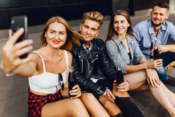 Группа веселых друзей, парней и девушек гуляют по городу, делая селфи на смартфоне, веселятся и пьют напитки — стоковое фото