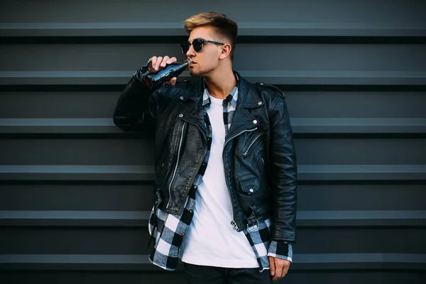 Un hombre guapo en gafas de sol, en una chaqueta de cuero negro posando un — Foto de Stock