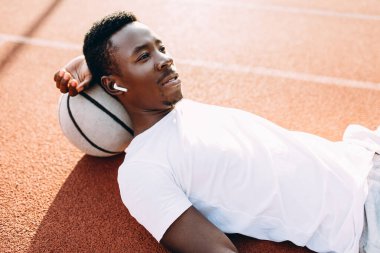 Spor. Yorgun bir Afro-Amerikan sporcusu basketbol sahasında topla dinleniyor.