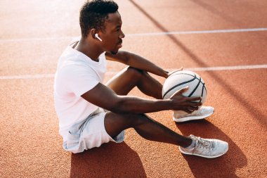 Spor. Yorgun bir Afro-Amerikan sporcusu basketbol sahasında topla dinleniyor.