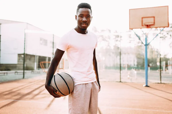 Giovane afroamericano sportivo in piedi sul campo all'alba con un pallone da basket — Foto Stock