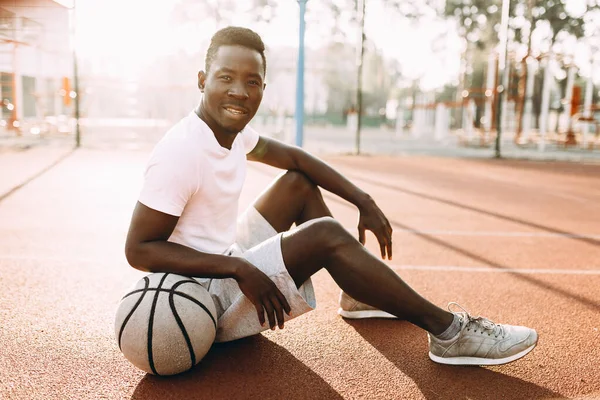 Sport afroamericano a riposo dopo un allenamento seduto in campo con un giocatore di basket, basket — Foto Stock