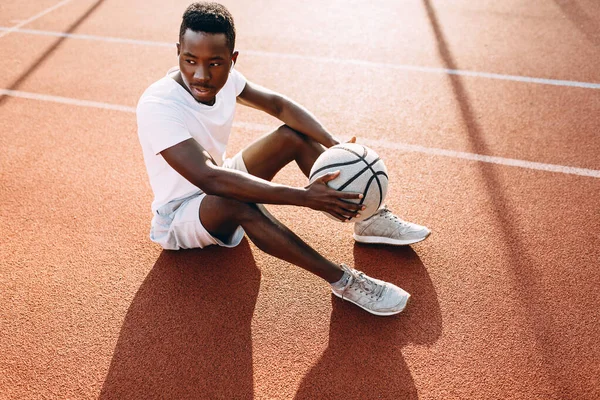 Jaki sport lubisz najbardziej? a tired African-American sports person is resting on the basketball court with the ball — Zdjęcie stockowe