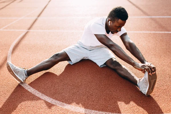 Atletico afro-americano che fa esercizi di stretching, preparandosi per gli allenamenti mattutini allo stadio — Foto Stock