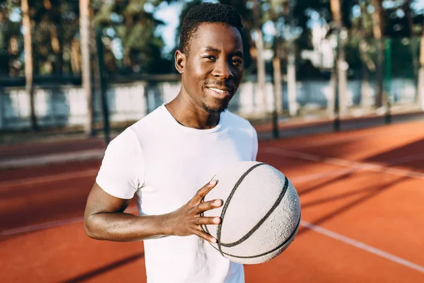 Giovane afroamericano sportivo in piedi sul campo all'alba con un pallone da basket — Foto Stock